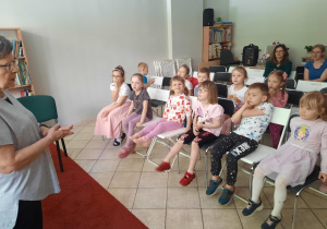 Dzieci siedzą na krzesłach i słuchają pani bibliotekarki.