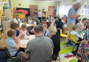 Rodzice i dzieci przy stolikach. Dzieci ozdabiają torebki na saszetki herbaty.