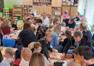 Dzieci wraz z rodzicami siedzą przy stolikach.