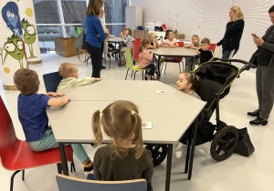Dzieci siedzą przy stoliku i słuchają.