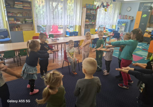 chłopiec świętuje urodziny, dzieci stoją w kole na granatowym dywanie i składają mu życzenia