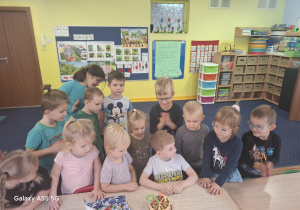 dziewcchłopiec siedzi za stolikiem, na którym widać symboliczny urodzinowy tort, za nim stoją dzieci