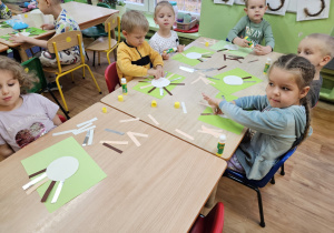 Dzieci siedzą przy stolikach i wykonują pracę plastyczną.