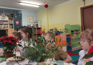 dzieci w odświętnych strojach siedzą przy stolikach, na których widać talerze ze smakołykami, ciastami, babeczkami.