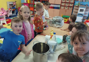 dzieci stoją przy stolikach, na stoliku widać produkty spożywcze, duży garnek