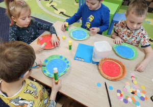 Dzieci wykonują pracę plastyczną przy stolikach.