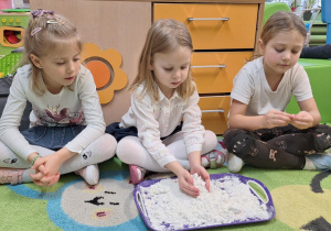 Dzieci siedzą na dywanie i oglądają sztuczny śnieg.