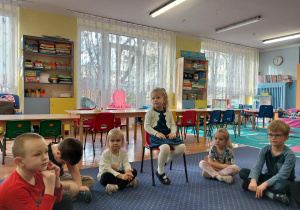 dziewczynka świętuje urodziny, siedzi na krzesełku, dookoła niej dzieci składają jej życzenia