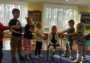 dziewczynka świętuje urodziny, siedzi na krzesełku, dookoła niej dzieci składają jej życzenia
