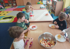 dzieci przy stolikach zjadają sałatkę owocową, którą mają na talerzach