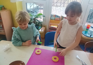 dzieci siedzą przy stolikach, kroją owoce na sałatkę