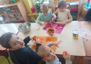 dzieci siedzą przy stolikach, kroją owoce na sałatkę