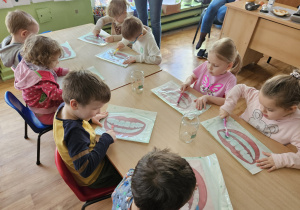 Dzieci siedzą przy stolikach i wykonują zadanie.