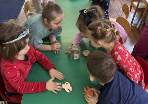 Dzieci siedzą przy stolikach i wykonują zadanie.