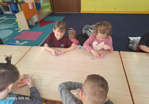 dzieci siedzą przy stolikach, lepią zęba z plastopianki