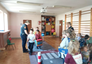 dzieci uczestniczą w zajęciach o bezpieczeństwie na sali gimnastycznej, poruszają się po drodze i po pasach zgodnie z przepisami ruchu drogowego