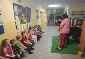 dzieci siedzą na ławeczce na korytarzu, pani trzyma na smyczy alpakę