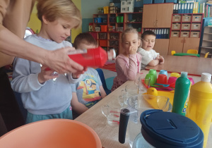 dzieci wykonują eksperymenty wykorzystując wodę, barwniki, cytrynę, sól, cukier, różne przedmioty