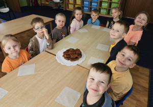 Dzieci siedzą przy stoliku na którym leży na talerzu pokrojone ciasto.