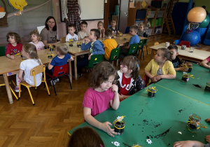 Dzieci siedzą przy stolikach.
