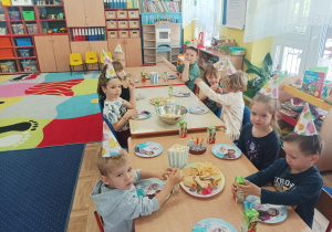 dziewczynka świętuje urodziny, dzieci siedzą przy stolikach, na których są słodycze, napoje, przekąski