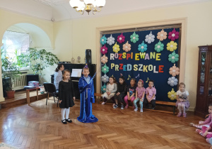 chłopiec i dziewczynka śpiewają piosenkę, pani akompaniuje im na pianinie
