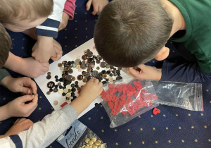 Dzieci siedzą w kole na dywanie i oglądają guziki.