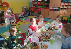 dzieci świętują wigilię klasową, siedzą przy stolikach, na których widać słodycze, owoce, soki