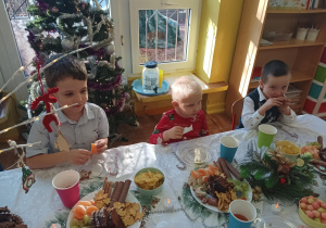 dzieci świętują wigilię klasową, siedzą przy stolikach, na których widać słodycze, owoce, soki