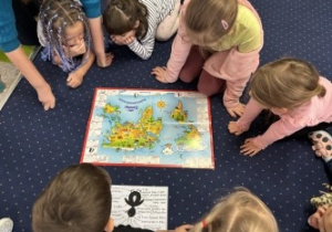 Dzieci siedzą w kole słuchając i obserwując mapę.