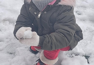 Dziecko bawi się śniegiem w ogrodzie.
