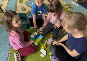Dzieci siedzą na dywanie i bawią się klockami Lego duplo.