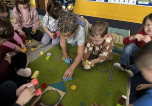 Dzieci siedzą na dywanie i bawią się klockami Lego duplo.