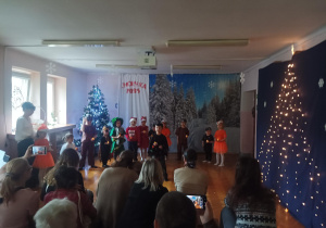 świateczny występ dzieci na sali gimnastycznej. dzieci mówią wiersze, śpiewają piosenki, rodzice oglądają występ.