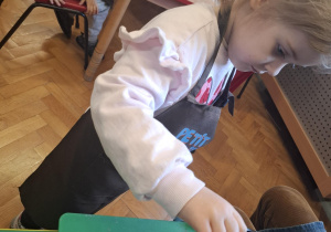 dzieci ubrane w brązowe fartuszki biorą udział w czekoladowych warsztatach, samodzielnie ozdabiają czekoladę w kształcie serca