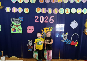 cgłopiec i dziewczynka pozują do zdjęcia na tle napisu Mini Olimpiada Gier Planszowych