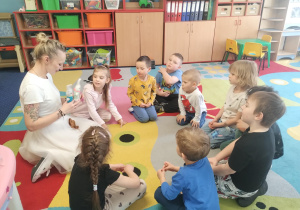 dzieci razem z panią siedzą w kole i przyglądają się królikom