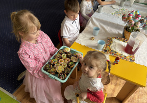 Dziewczynka częstuje dzieci babeczkami przygotowanymi wraz z mamą i siostrą.
