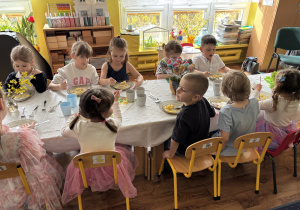 Dzieci siedzą przy stołach i zjadają wielkanocny obiad.