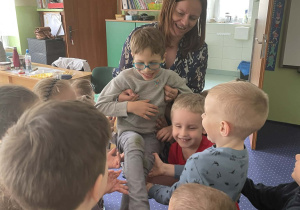 Dzieci wraz z nauczycielem podrzucają chłopca.