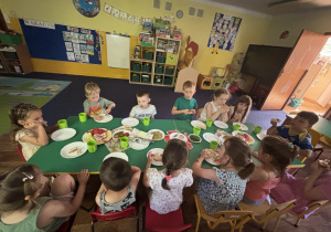 Dzieci siedzą przy stole i jedzą śniadanie.