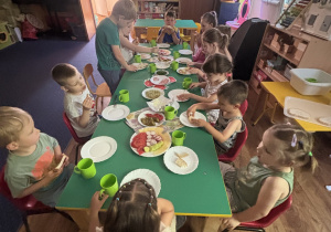 Dzieci siedzą przy stole i jedzą śniadanie.