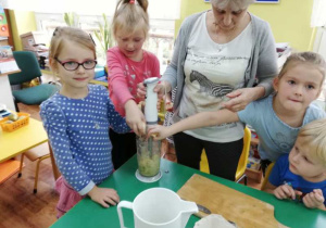 Dziewczynki blendują pokrojone owoce wraz z panią Ewą.