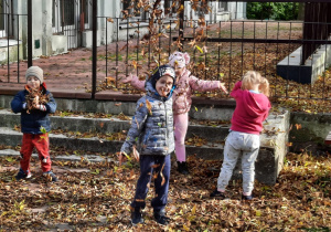Dzieci bawią się liśćmi w ogrodzie przedszkolnym.