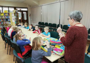 Pani bibliotekarka pokazuje różne rodzaje kart bibliotecznych.