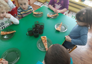 Dzieci siedzą przy stole. Na talerzykach leżą kawałki pizzy.