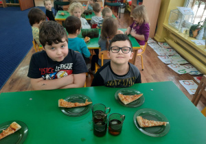Dzieci siedzą przy stole. Na talerzykach leżą kawałki pizzy.