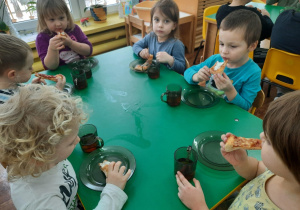 Dzieci siedzą przy stole. Na talerzykach leżą kawałki pizzy.