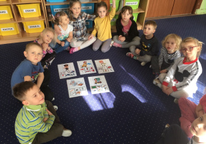 Dzieci siedzą w kole na dywanie i prezentują wykonaną pracę. Przyporządkowały atrybuty do zawodów.