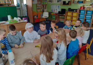 Dzieci siedza przy stołach, na których znajdują się produkty do wykoania koktajlu.